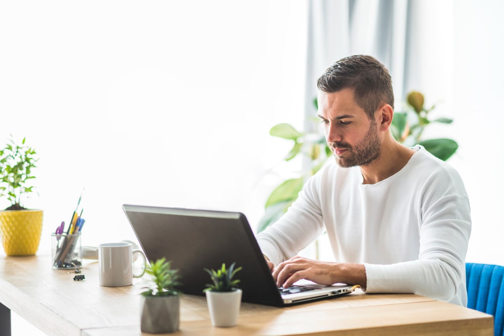 A Man Engaged With His Laptop At A Desk, Representing The Ease Of Simplified Payment Processes